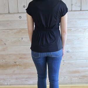 Puede incluir: Una camisa negra de manga corta con cintura ajustada y corte holgado. La camisa se lleva con jeans azules.