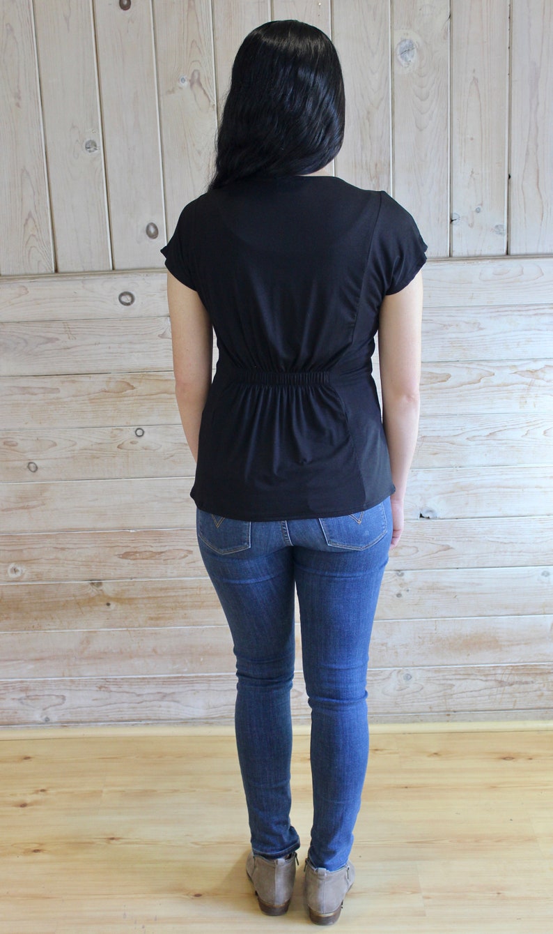 Puede incluir: Una camisa negra de manga corta con cintura ajustada y corte holgado. La camisa se lleva con jeans azules.