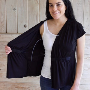 Puede incluir: Una cubierta de lactancia negra con un top blanco debajo. La cubierta tiene un cierre de bot&oacute;n y una cintura con cord&oacute;n. La cubierta est&aacute; abierta en la parte delantera, revelando el top.