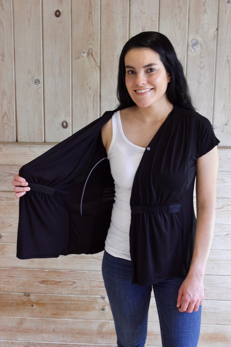 Puede incluir: Una cubierta de lactancia negra con un top blanco debajo. La cubierta tiene un cierre de bot&oacute;n y una cintura con cord&oacute;n. La cubierta est&aacute; abierta en la parte delantera, revelando el top.