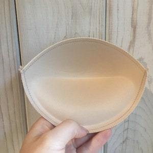 Puede incluir: Un inserto de copa de sujetador beige con un borde cosido.