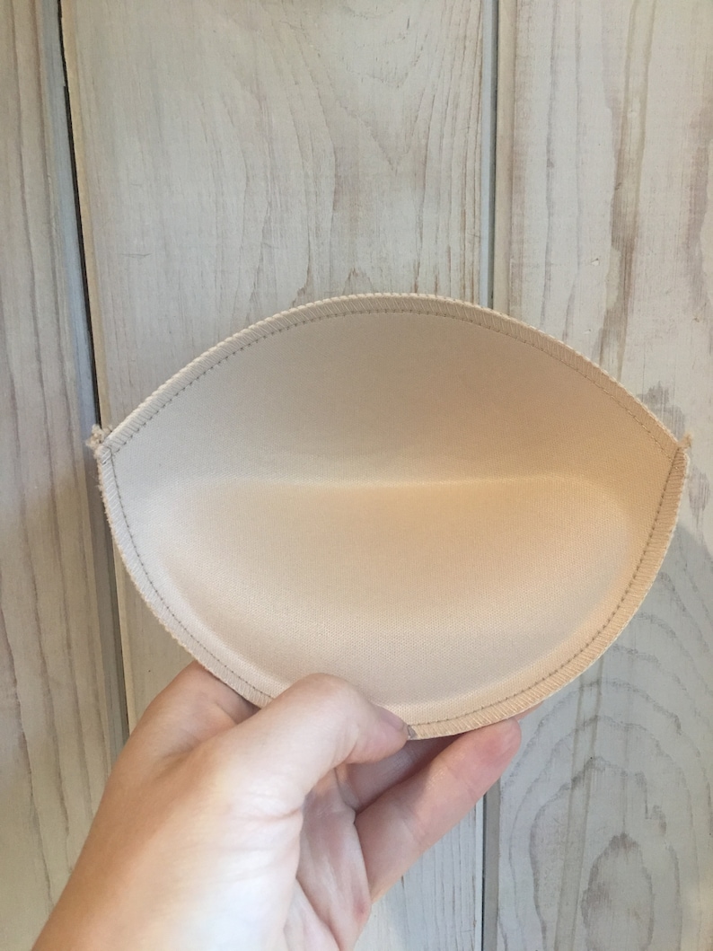 Puede incluir: Un inserto de copa de sujetador beige con un borde cosido.