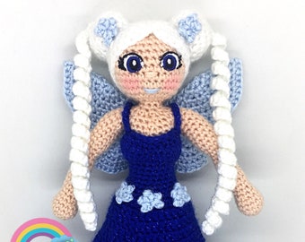 May include: A crocheted fairy doll with white hair, blue wings, and a blue dress with white stars. The doll is holding a white wand.