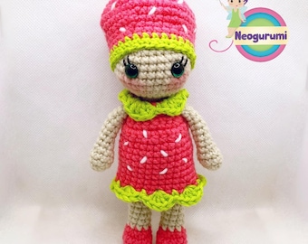 May include: A handmade crochet doll dressed as a strawberry. The doll has a pink strawberry hat with white seed details, a matching dress, and red shoes. The doll has a green collar and eyelashes. The doll is made of beige and red yarn.