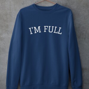 K&ouml;nnte beinhalten: Ein marineblauer Pullover mit dem Aufdruck "I'M FULL" in Wei&szlig; auf der Vorderseite.
