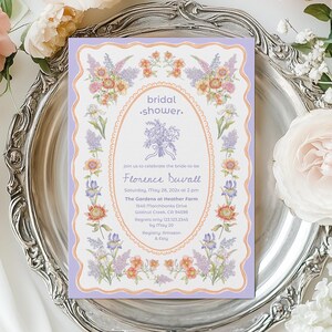 May include: A rectangular bridal shower invitation card with a scalloped lavender border and an oval center frame. The card features floral illustrations of purple lilacs and orange flowers, with text detailing the event for Florence Duvall.