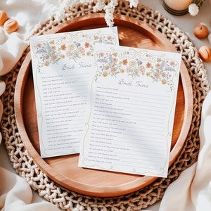May include: Two printable bride trivia game cards with floral borders. The cards have questions about the bride's favorite things, childhood, and more. The cards are on a wooden tray with a woven placemat.
