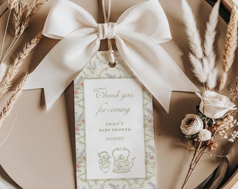 May include: A white satin bow tied around a string attached to a thank you tag. The tag has a floral border and says "Thank you for coming, Emily's Baby Shower 10/10/2027".