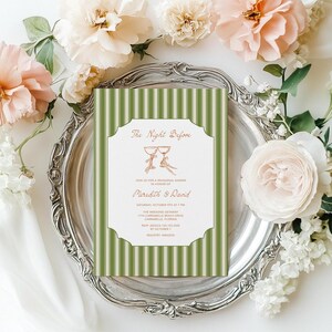 May include: A wedding rehearsal dinner invitation with a green and white striped background. The invitation features the text "The Night Before" and the names "Meredith & David" in a decorative font. The invitation is on a silver platter surrounded by flowers.
