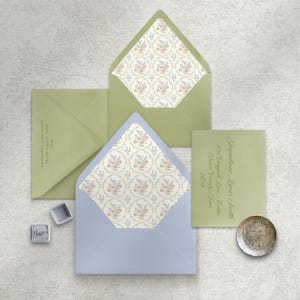 May include: A collection of wedding stationery, including light green and blue envelopes with floral patterned liners. A small silver dish and two ring boxes are also present. The text on the envelopes reads "806 Chappell Lane, Austin, Travis County, Texas".