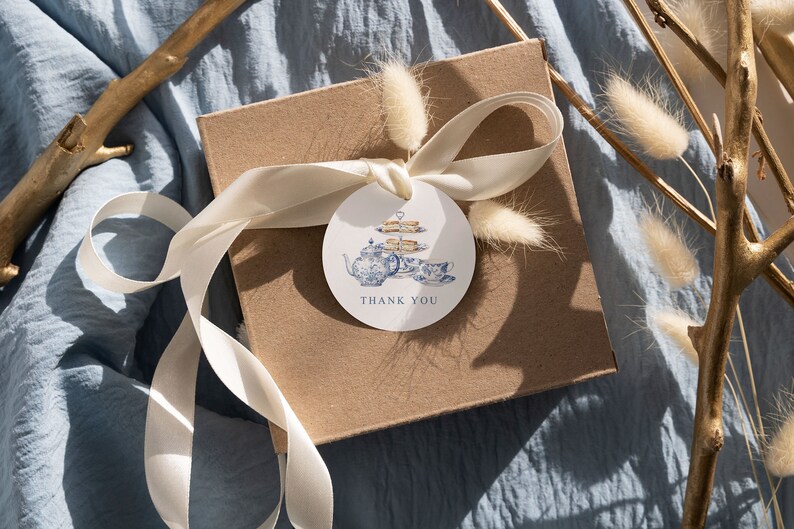 May include: A brown gift box with a white ribbon and a round thank you tag. The tag features a blue and white teapot with a tiered cake stand and the text "Thank You".