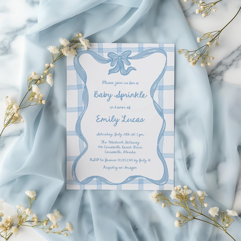 Peut inclure: Une invitation de f&ecirc;te pr&eacute;natale bleu et blanc avec un n&oelig;ud en ruban bleu et le texte "Veuillez vous joindre &agrave; nous pour un Baby Sprinkle en l'honneur d'Emily Lucas". L'invitation comprend la date, l'heure, le lieu et les informations RSVP.