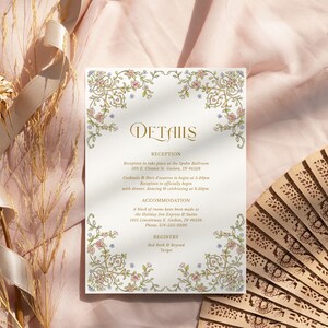 May include: A rectangular wedding details card featuring gold, pink, and blue floral scrollwork borders. The text reads Details, Reception, Accommodation, and Registry, with specific event information and addresses printed in a gold serif font.