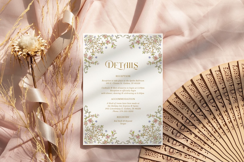 May include: A rectangular wedding details card featuring gold, pink, and blue floral scrollwork borders. The text reads Details, Reception, Accommodation, and Registry, with specific event information and addresses printed in a gold serif font.
