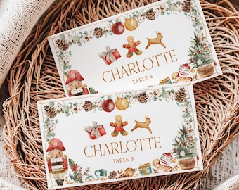 May include: Two rectangular white place cards featuring a watercolor Christmas border with pinecones, ornaments, a gingerbread person, a reindeer, a nutcracker, and a tree. The text reads CHARLOTTE and TABLE 6 in gold lettering.
