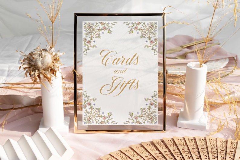 Op de afbeelding: Een gouden lijst met een witte achtergrond en een bloemige rand. Het bord heeft de tekst "Kaarten en Geschenken" in gouden letters.