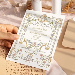 以下が含まれることがあります： ピンク、ブルー、グリーンの色合いの花柄のデザインが施された「Save the Date」カード。カードには金色のフレームと「Save the Date for the wedding of Heredith and David」というテキストが書かれています。