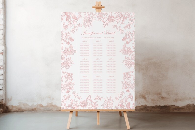 May include: A rectangular wedding seating chart sign on a wooden easel featuring a white background with dusty pink botanical illustrations along the borders. The text reads Jennifer and David, San Francisco, California, April 10, 2025, and table lists.
