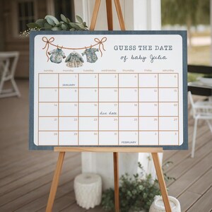 A vertical baby shower due date calendar game poster template card displaying custom text inside a blue striped border decorated with a watercolor clothesline.