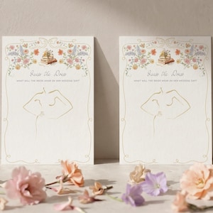 May include: Two identical rectangular paper cards featuring a gold-toned line drawing of a torso. The text reads Guess the Dress and What will the bride wear on her wedding day? The top border displays a watercolor illustration of flowers and books.