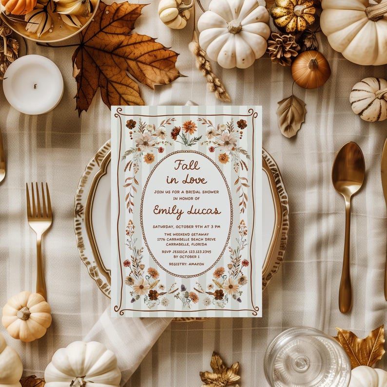May include: A bridal shower invitation with the text "Fall in Love" in an oval floral frame. The invitation is on a plate with gold cutlery, surrounded by pumpkins, leaves, and candles.