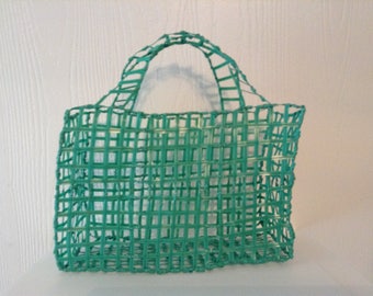 May include: A teal blue woven plastic tote bag with a handle. The bag is made of a grid pattern of woven plastic.