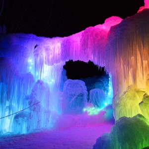 Pode incluir: Uma vibrante estrutura de gelo iluminada com um arco-íris de cores. O arco é formado por estalactites, com um fundo escuro. A cena é iluminada com luzes azuis, roxas, rosas, amarelas e verdes, criando um mágico país das maravilhas de inverno.