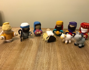 May include: A nativity scene set with crocheted figures including a baby Jesus, Mary, Joseph, an angel, a shepherd, three wise men, a sheep, and a donkey.