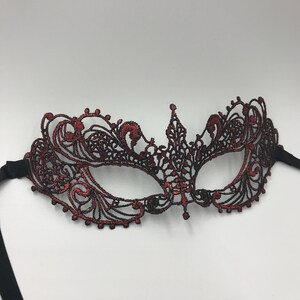 May include: A red lace masquerade mask with black ribbon ties. The mask has a delicate, intricate design.