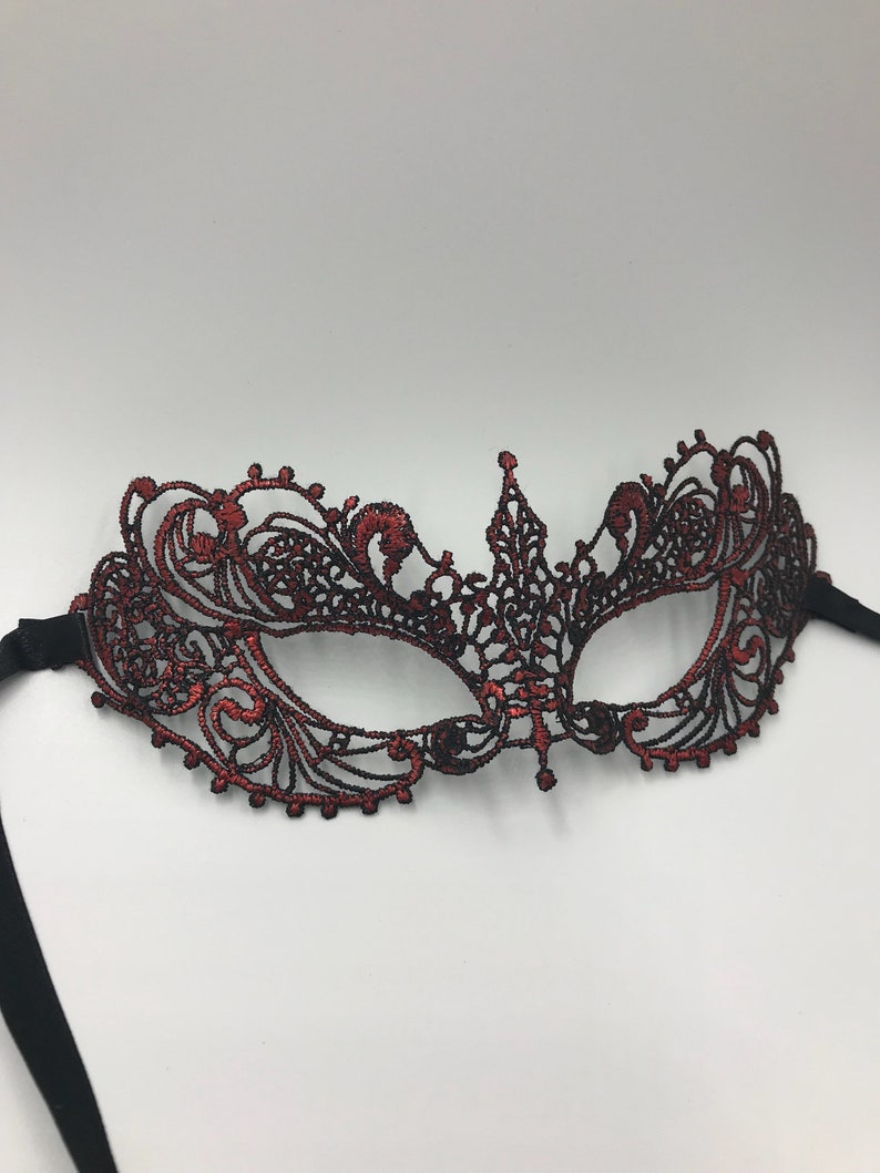 May include: A red lace masquerade mask with black ribbon ties. The mask has a delicate, intricate design.