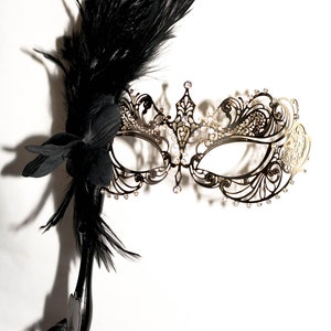 Gold masquerade mask with a stick mask handle with black feathers. masquerade lace metal mask. wedding masquerade mask