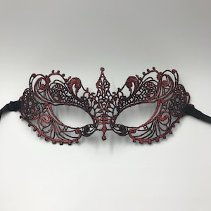 May include: A red and black lace masquerade mask with intricate details. The mask has a delicate design and is perfect for a costume party or a night out.
