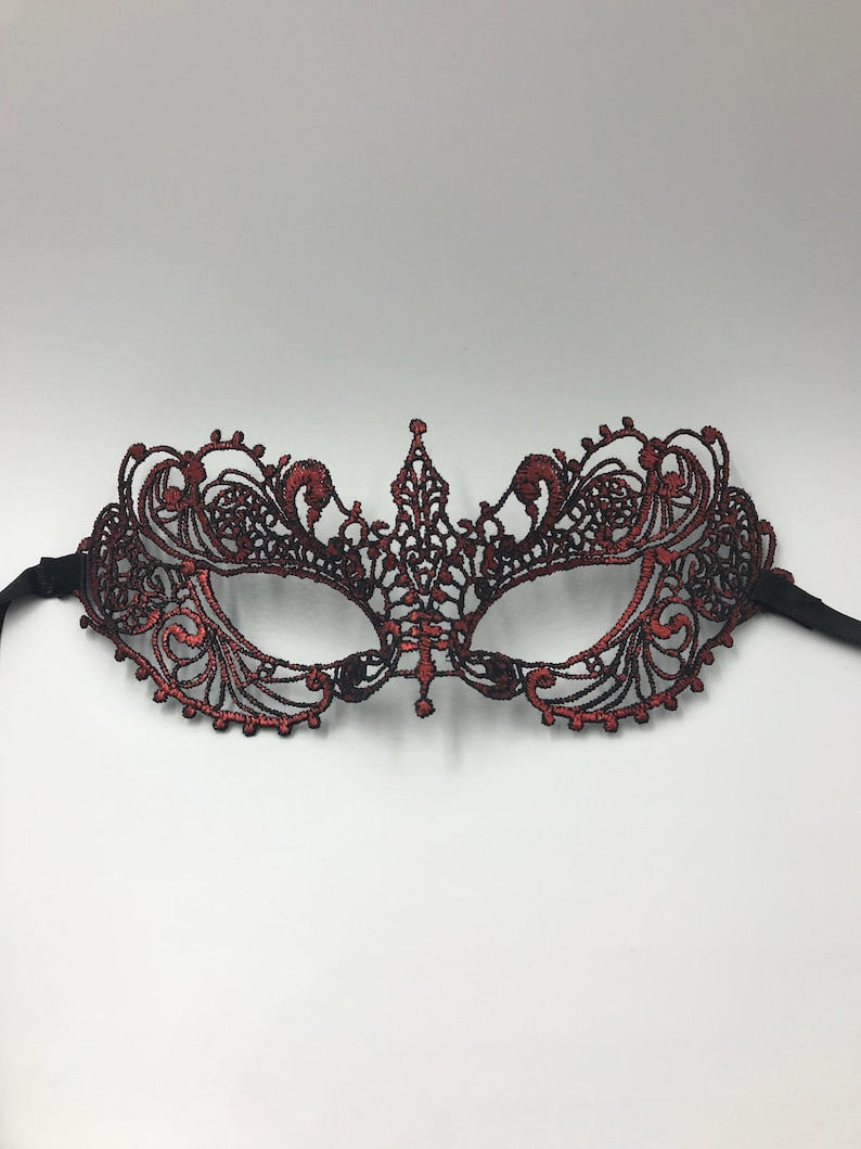 May include: A red and black lace masquerade mask with intricate details. The mask has a delicate design and is perfect for a costume party or a night out.