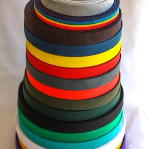 Puede incluir: Una pila de correas de tejido de colores en varios colores, incluyendo gris, marr&oacute;n, azul, amarillo, rojo, verde, negro, blanco, naranja y morado.