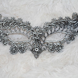 May include: A black lace masquerade mask with silver accents. The mask has a delicate, intricate design and is perfect for a costume party or a night out.