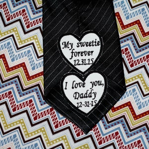 May include: A black striped tie with two white heart-shaped patches sewn on. The top patch says "My sweetie forever 12.31.15" and the bottom patch says "I love you, Daddy 12-31-15".