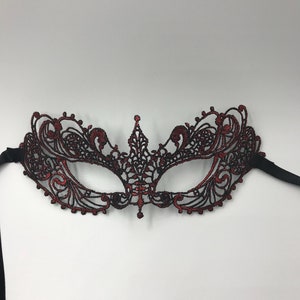 May include: A red and black lace masquerade mask with intricate details. The mask has a delicate design and is perfect for a costume party or a night out.