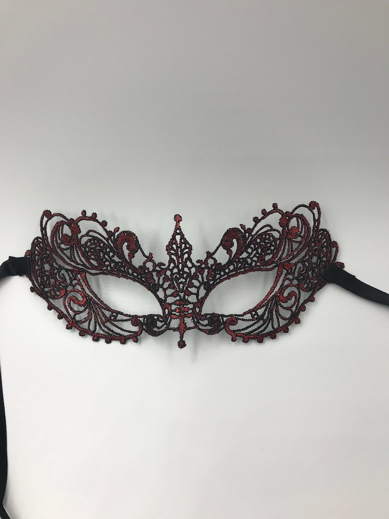 May include: A red and black lace masquerade mask with intricate details. The mask has a delicate design and is perfect for a costume party or a night out.