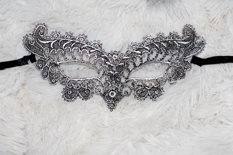 May include: A silver lace masquerade mask with a black ribbon attached. The mask has a delicate, intricate design.