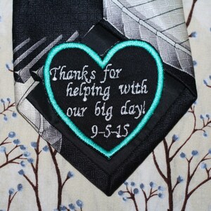 May include: A black tie with a turquoise heart-shaped patch that says "Thanks for helping with our big day! 9-5-15".