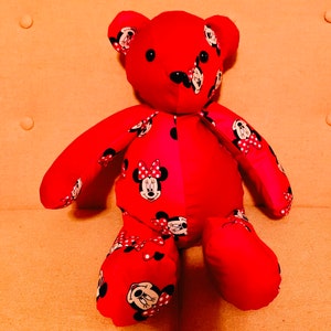 Op de afbeelding: Rode pluche teddybeer met een Minnie Mouse print. De beer zit op een licht oranje bank. De tekst "Stefanelbeadwork" is zichtbaar in het midden bovenaan de afbeelding.
