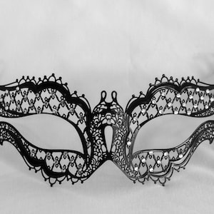 Op de afbeelding: Zwart filigraan maskerademasker met een delicaat, opengewerkt ontwerp. Het masker heeft een symmetrisch patroon met sprankelende versieringen. Een zwart lint is bevestigd om het masker vast te zetten.