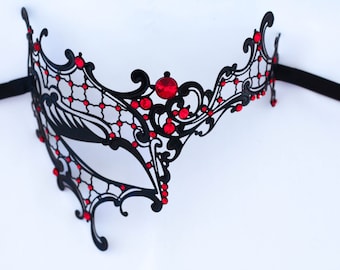 May include: A black masquerade mask with a delicate, intricate design. The mask is adorned with red rhinestones and has a single eye opening.