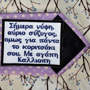 May include: A purple tie with a white embroidered patch that reads "Today bride, tomorrow wife, but always my little girl. With love, Kalliope."