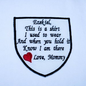 Puede incluir: Un parche de tela blanca con texto bordado en negro que dice "Ezekiel, This is a shirt I used to wear And when you hold it Know I am there Love, Mommy". Un corazón rojo bordado está debajo del texto.
