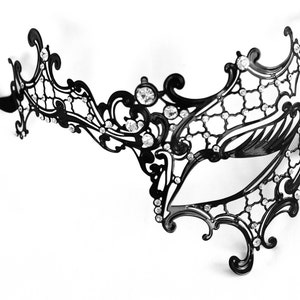 May include: A black masquerade mask with intricate, ornate details and rhinestones. The mask has a single eye opening and is attached to a black ribbon.