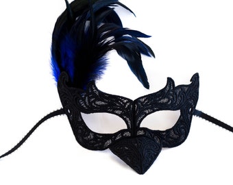 May include: A black lace masquerade mask with a blue and black feather accent. The mask has a long black ribbon tie.