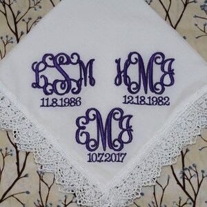 May include: White handkerchief with lace trim and purple embroidered monograms and dates. The monograms are "SM" with the date "11.8.1986", "KMC" with the date "12.18.1982", and "MC" with the date "10.7.2017".