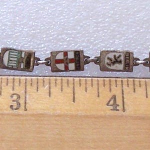Peut inclure: Bracelet vintage compos&eacute; de maillons rectangulaires orn&eacute;s de divers motifs &eacute;maill&eacute;s color&eacute;s. Le bracelet mesure environ 18 cm de long et est plac&eacute; &agrave; c&ocirc;t&eacute; d'une r&egrave;gle. Les maillons sont reli&eacute;s par de petits anneaux m&eacute;talliques.