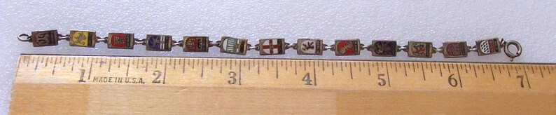 Peut inclure: Bracelet vintage compos&eacute; de maillons rectangulaires orn&eacute;s de divers motifs &eacute;maill&eacute;s color&eacute;s. Le bracelet mesure environ 18 cm de long et est plac&eacute; &agrave; c&ocirc;t&eacute; d'une r&egrave;gle. Les maillons sont reli&eacute;s par de petits anneaux m&eacute;talliques.
